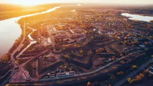 Saulrieta panorāma pār Daugavpili, izceļot pilsētas arhitektūru un Daugavas upes plūdumu.