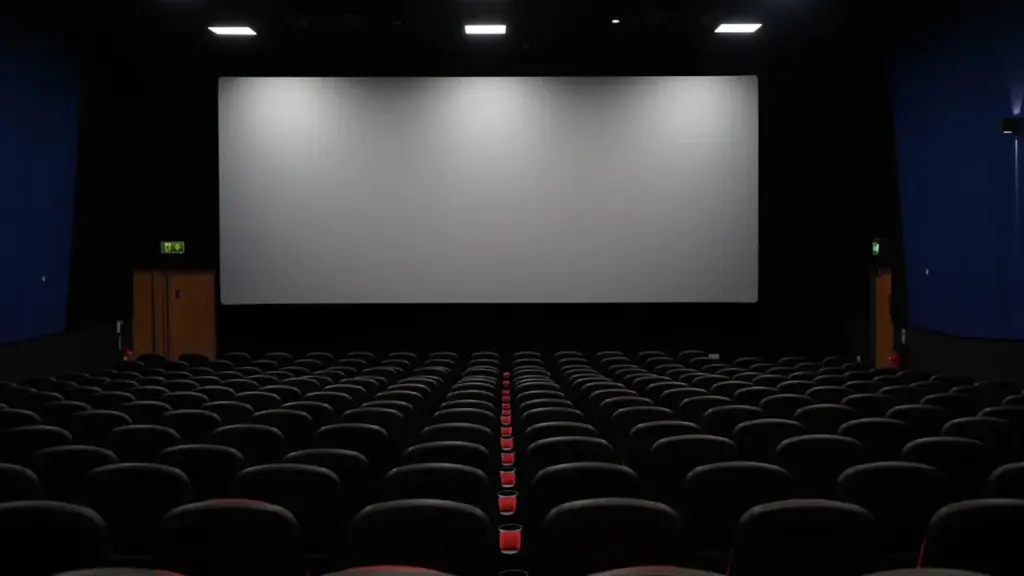 Tukšas kinoteātra skatītāju zāles rindas ar sarkanīgiem krēsliem pirms filmu seansa sākuma.