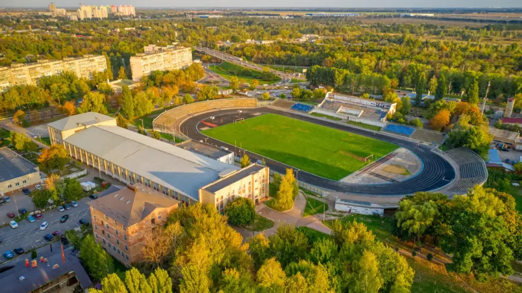 Skolas stadiona sporta laukums no augšas ar zaļu zāli un skriešanas celiņiem