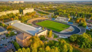 Skolas stadiona sporta laukums no augšas ar zaļu zāli un skriešanas celiņiem